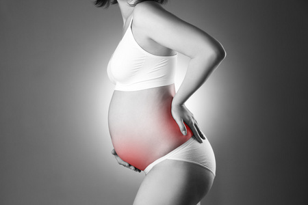 白种人孕妇在白色内衣与背部和灰色演播室背景上的腹部疼痛