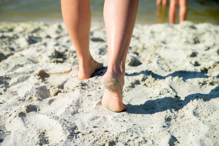 女人的腿闭上了在沙滩上散步。度假理念