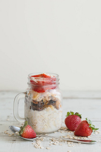 隔夜燕麦在一个罐子里放着草莓的木桌, 垂直的照片。健康早餐食谱与水果, 全谷物和牛奶