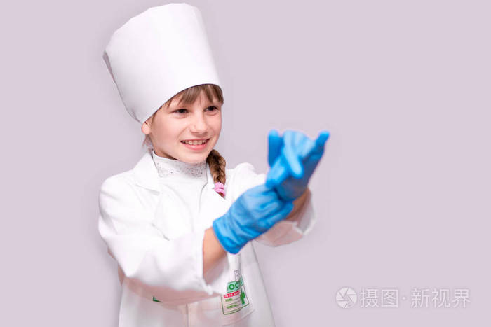 微笑的小女孩在医疗制服和蓝色手套看在白色的相机隔离