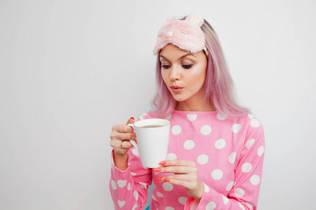 穿着粉红色睡衣和睡面具的迷人女孩享受早晨的咖啡
