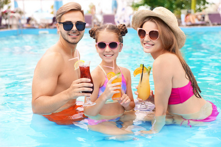 快乐的家庭与鸡尾酒在游泳池在阳光明媚的一天