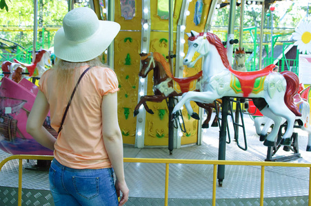 一个在游乐园的草帽的女孩看着旋转木马