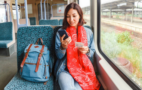 坐在靠窗的火车旁的年轻快乐女子使用智能手机