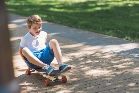 高角度看可爱的微笑男孩坐在滑板在公园