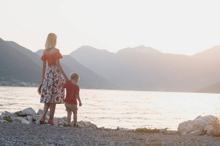 在黑山夕阳下看海的红色 t恤衫的母亲和儿子的背面视图