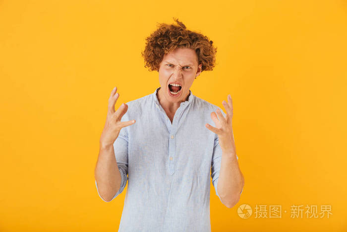 愤怒的愤怒的人的照片20s 与卷曲的头发举手在黄色背景的刺激隔离
