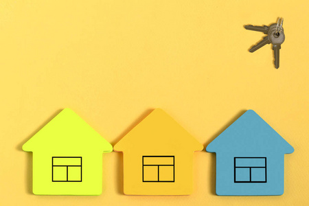 在黄色背景下, 带有图片窗口和键的房屋形状的便笺的彩色纸块.