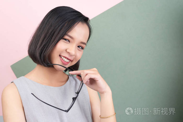 美丽的亚洲年轻女子的肖像手持眼镜和微笑在相机上