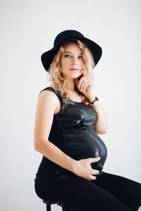 时尚的孕妇在黑色的帽子和闪闪发光的顶部拥抱她的肚子