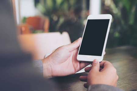 手机空白的白色屏幕,木制的桌子上杯热咖啡,在咖啡馆里的样机形象照片