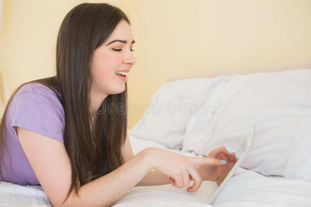 在卧室里用平板电脑躺在床上的快乐的黑发女人