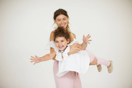 年轻的微笑的母亲抱着欢快的小女儿快乐地玩在飞行飞机在白色背景