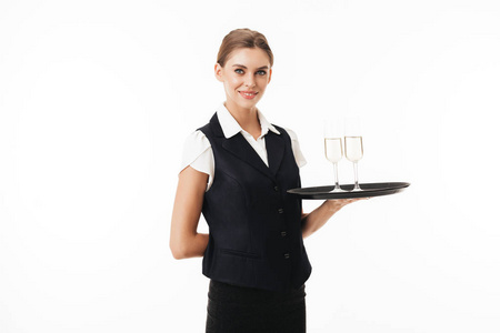 年轻的微笑的女服务员在制服持有托盘与眼镜朦胧地看着在白色背景相机