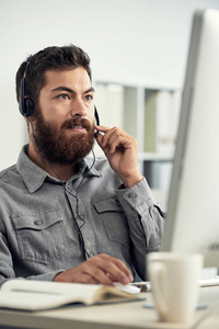 在电话销售中心工作的大胡子男子, 并与客户在耳机发言
