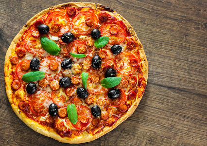比萨配有芝士干酪, 意大利腊肠, 胡椒粉, 意大利香肠, 西红柿, 橄榄, 香料和新鲜罗勒。意大利比萨的木质背景。复制空间。顶部