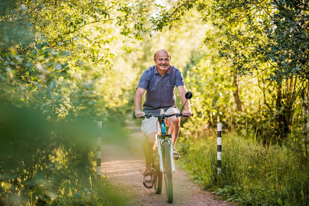 快乐的老人骑自行车在一个美丽的阳光明媚的一天公园。老年的活跃生活。体育的概念在假期