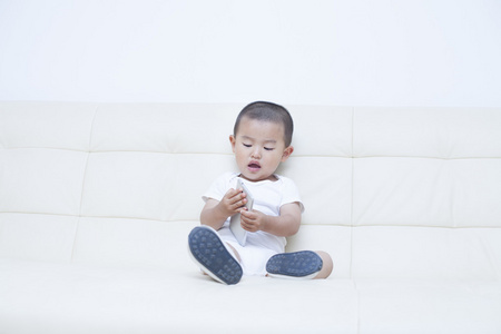 可爱的中国小男孩在沙发上玩手机