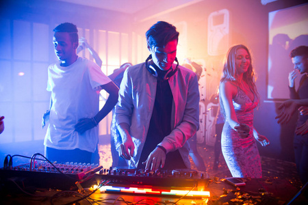 在混音器的帮助下演奏时尚音乐, 而快乐的朋友则在他身后跳舞, 现代夜
