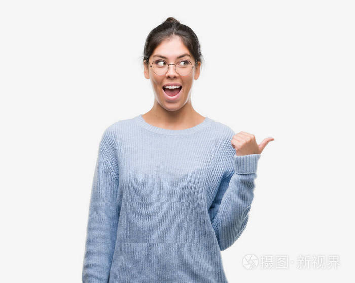 年轻漂亮的西班牙裔女子穿着一个包子指向和显示与拇指与快乐的脸微笑