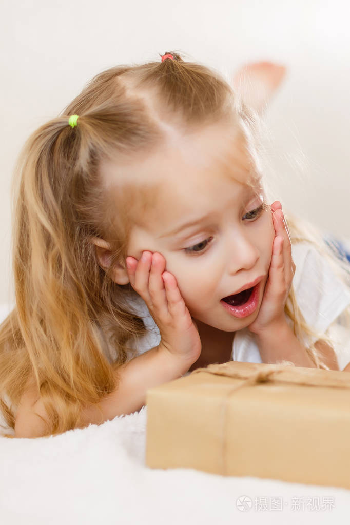 惊奇的小女孩躺在床上看礼品盒