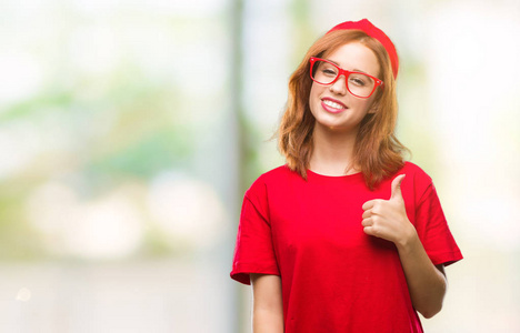 年轻美丽的女人在孤立的背景下做快乐大拇指手势与手。批准表达式看相机与显示成功