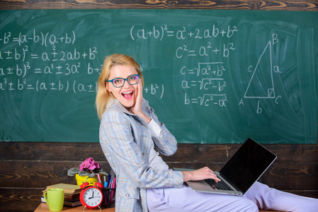 女教师持有笔记本电脑坐桌教室黑板背景。女讲师知道如何保持现代时代的联系。现代一代的老师。非正规环境效益研究