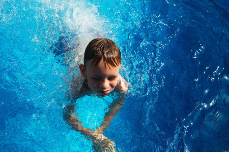 快乐的孩子玩在游泳池上一个热带度假胜地在海蓝色的水中。夏季度假概念。可爱的男孩在泳池里的水中游泳。溅和乐趣在游泳池里的孩子
