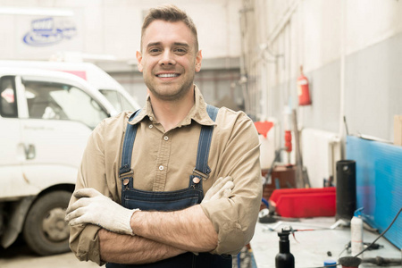 年轻有吸引力的白种男性汽车技术员的肖像站在维修车间和微笑在相机愉快地