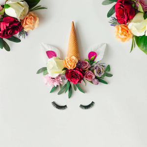 创意安排的独角兽头与五颜六色的花朵和冰淇淋锥分离的白色背景。夏日童话的最小艺术幻想观