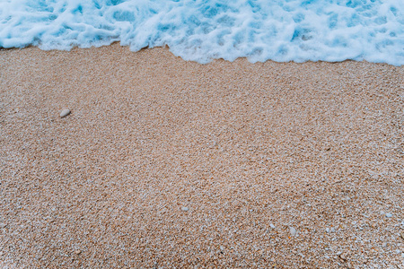 卵石滩上蓝绿松石海水的滚动软泡沫波的形状。背景。顶部视图