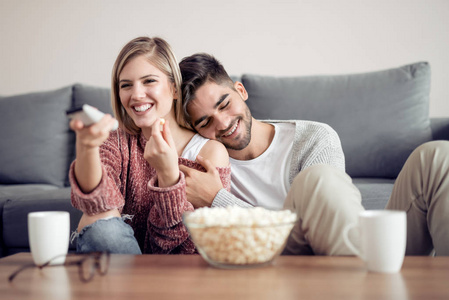年轻夫妇在他们的公寓放松, 坐在沙发上, 看电影和吃爆米花