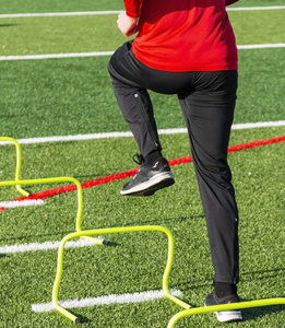 一名高中运动员正在执行速度和敏捷的运动训练演习踏过黄色迷你跨栏在一个绿色草皮领域