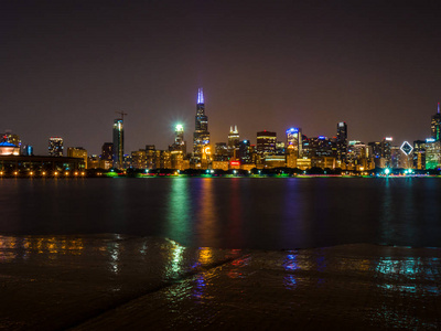 美丽的长曝光芝加哥夜天际线照片与五颜六色的红色, 绿色, 紫色, 蓝色, 橙色, 和黄色建筑灯和水的反射在密歇根湖和海岸线的前景