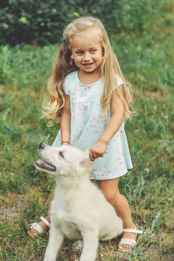 小可爱的金发女孩玩她的小狗金色猎犬在夏天在公园里