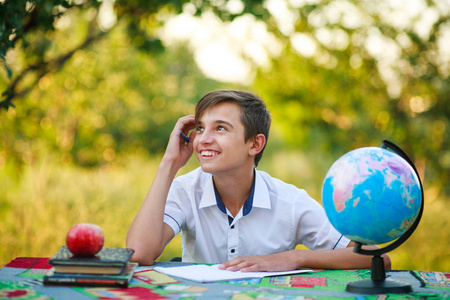 沉思的小学生在室外花园的餐桌上看书, 微笑着看着。学校概念。返回学校