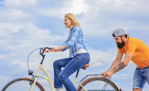 支持有助于相信自己。支持和友谊。女人骑自行车的天空背景。男人帮助保持平衡骑自行车。女孩骑自行车, 而男人支持她。服务和协助