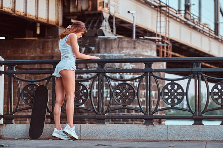 后视图的感官溜冰的女孩穿着短裤和 t恤靠在堤防上的护栏