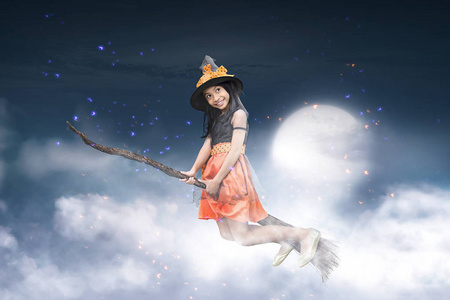 愉快的亚洲巫婆女孩飞行在扫帚与月光背景
