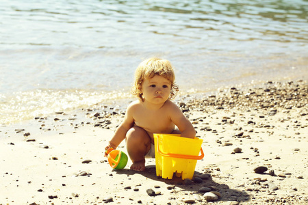 小好奇滑稽的金发男孩坐在海海岸海滩与波浪水