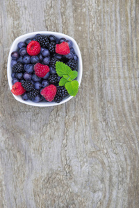 蓝莓, 黑莓, 红莓混合在老木桌背景白色碗里