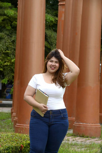 亚洲漂亮笑脸脸胖女人的肖像站在公园里的柱子上拿着一本小册子