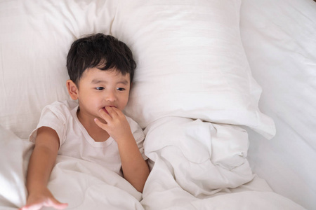 3岁的小生病或生病的亚洲男孩在家里的床上, 悲伤的孩子躺在白色的床上, 枕头和毯子, 顶部视图与复制空间添加文本