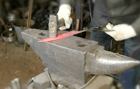 在锻造时用金属做刀子。关闭铁匠手击中热金属与一个大锤子在铁砧上