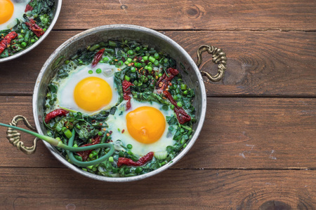 绿色 shakshuka。鲜菠菜煎蛋, ramson, 韭菜在灰色背景下的平底锅, 顶部视图