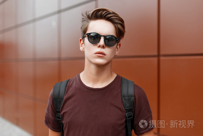 年轻的帅小伙,头发中站在一堵墙附近的太阳镜