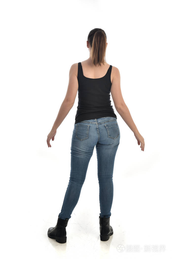 穿黑色单和牛仔裤的黑发女孩的全长肖像.站姿, 回到相机.