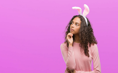 年轻的西班牙裔妇女穿着复活节兔子耳朵严肃的面孔思考问题, 非常困惑的想法