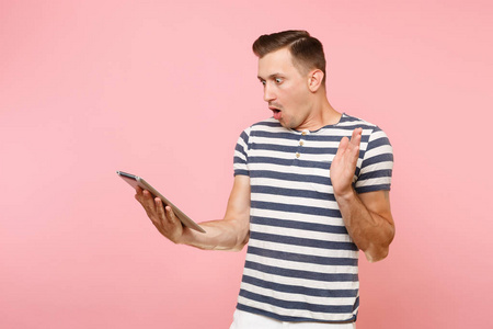 震惊的肖像惊讶的用户男子在条纹 t恤上工作的平板电脑电脑隔离在柔和的粉红色背景。人们真挚的情感生活理念。复制空间上的广告区域