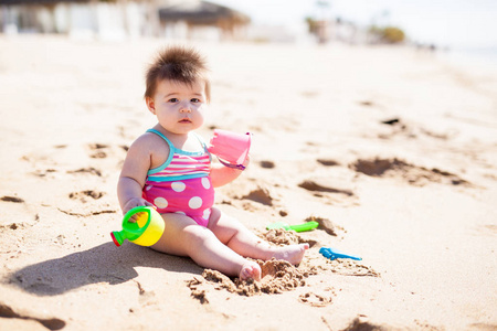 小女孩穿着泳衣在阳光明媚的沙滩上玩沙子和水桶